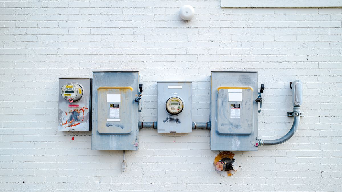 Plusieurs compteurs électriques et boîtiers fixés sur un mur de briques blanchi, vus de face