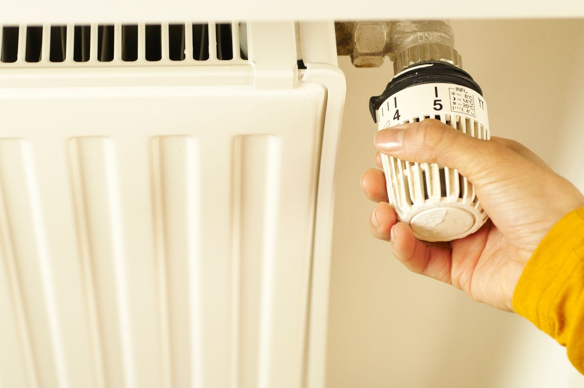 Main qui tourne le robinet thermostatique d’un radiateur