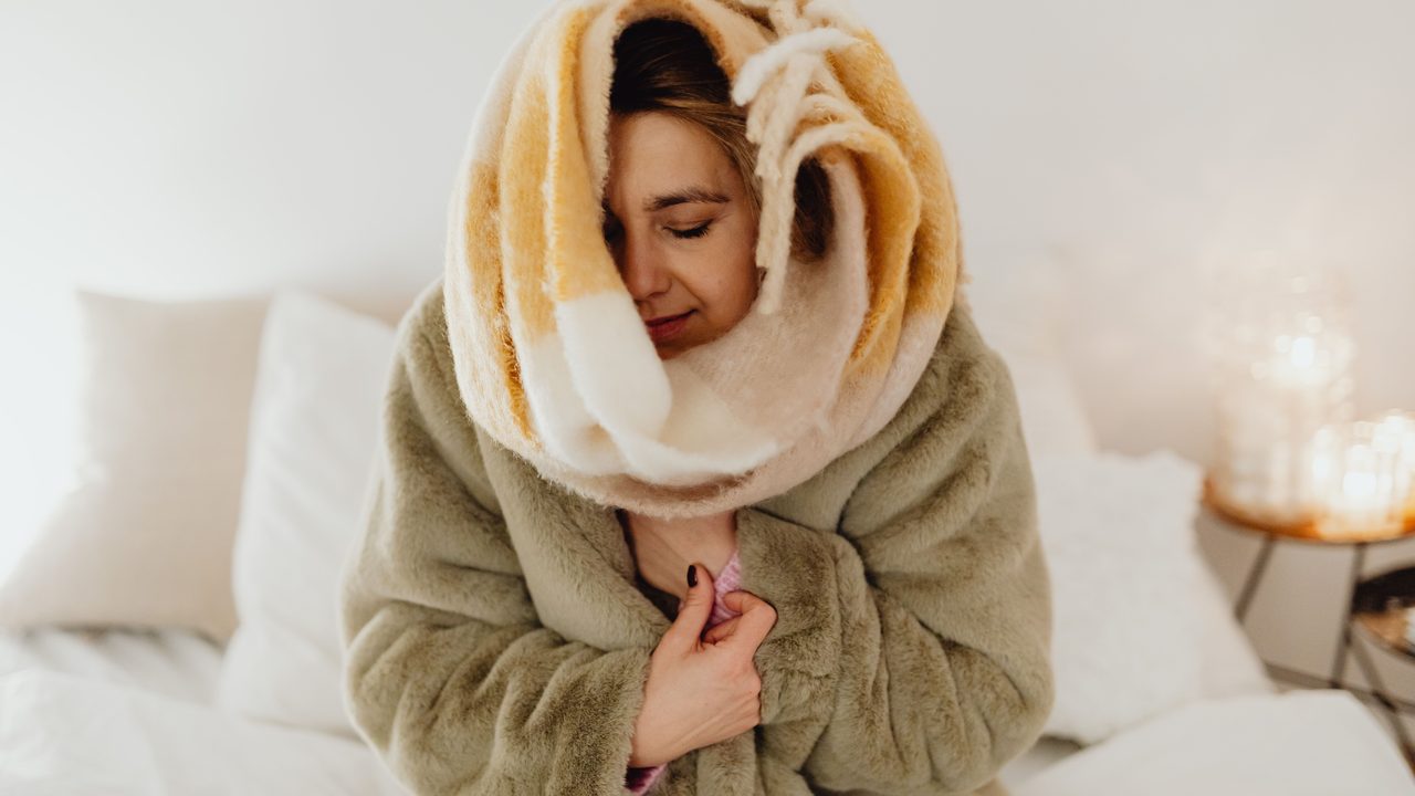 Femme emmitouflée dans une couverture et un manteau, dans un logement froid